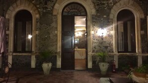 An entrance with three arched doorways, a dark interior visible through the central doorway, and potted plants on either side.