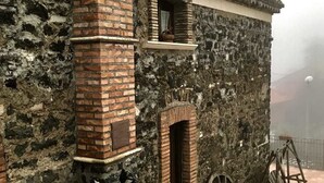 A rustic stone building with a brick chimney, a small window, and a large wooden wheel.