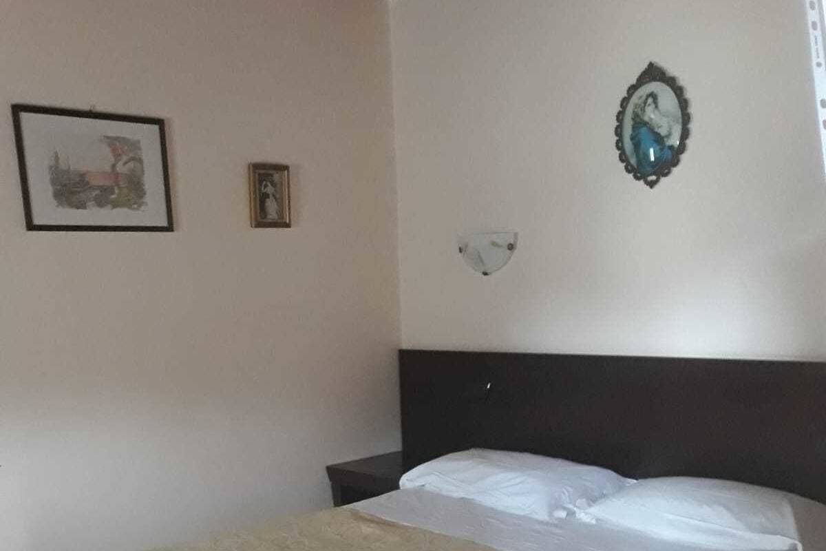 Une chambre à coucher avec un lit, une table de chevet, une lampe fixée au mur et un tableau encadré.