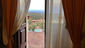 An open doorway with curtains, leading to a balcony with a view of a swimming pool and buildings.