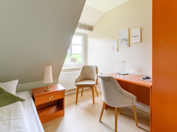 A modern hotel room with a bed, a desk, a chair, a nightstand, and a window with a view. - Nordsee-Hotel Arlau-Schleuse (Hattstedtermarsch)
