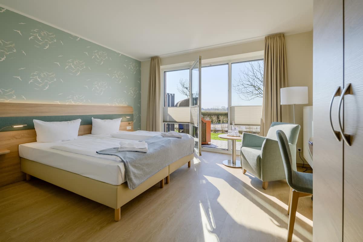 Habitación de hotel con una cama grande, un escritorio con silla, una ventana con vistas al exterior y una lámpara.