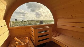 Una sauna de madera con un amplio ventanal en arco, bancos de madera y un balde de madera.