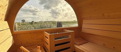A wooden sauna with a large arched window, wooden benches, and a wooden bucket.