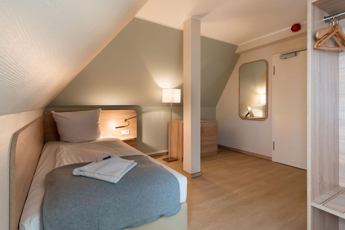 Un dormitorio con cama, mesita de noche, lámpara y un espejo en la pared.