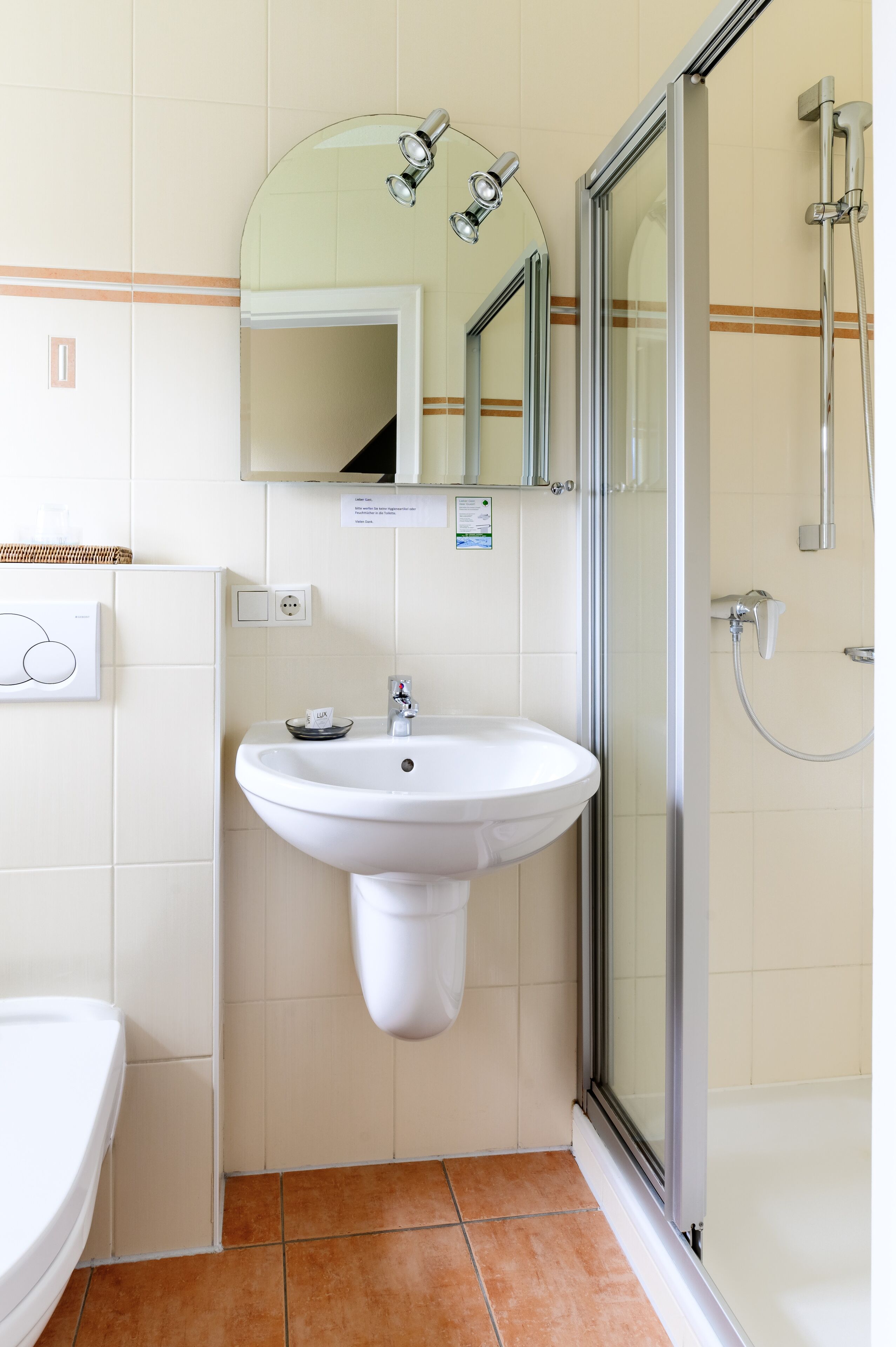 Un baño con lavamanos blanco, espejo y ducha con mampara de vidrio.