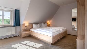 Een moderne slaapkamer met een schuine kap, een groot bed met witte lakens, twee bedlampen, een houten nachtkastje en uitzicht op het buitenlands landschap door een raam met blauwe gordijnen.