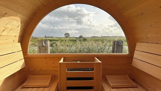 Una sauna de madera con un amplio ventanal de arco que da a un campo.