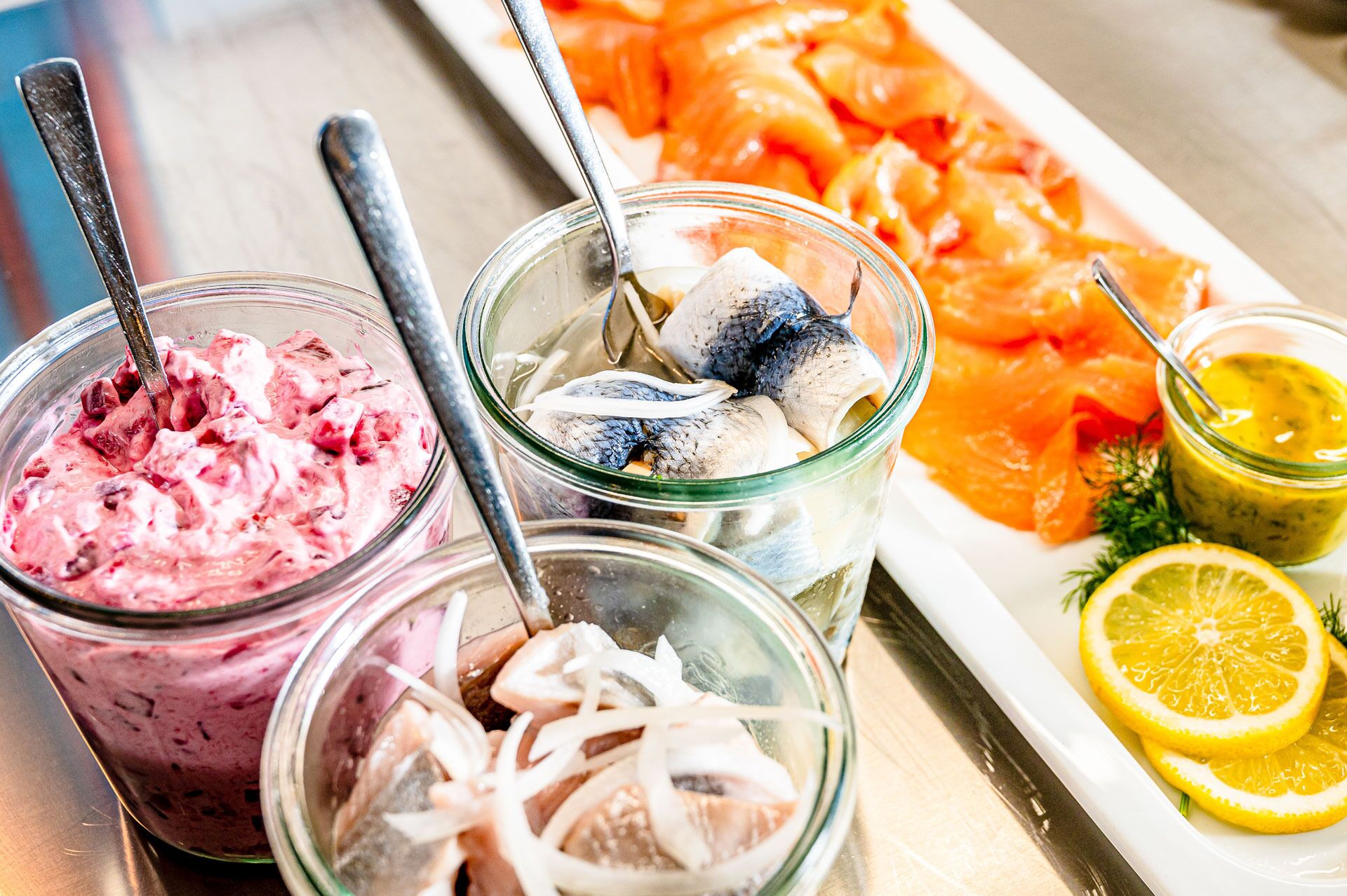 Een tafel met diverse etenswaren, zoals zalm, ingelegde haring en drankjes met bessenaroma.