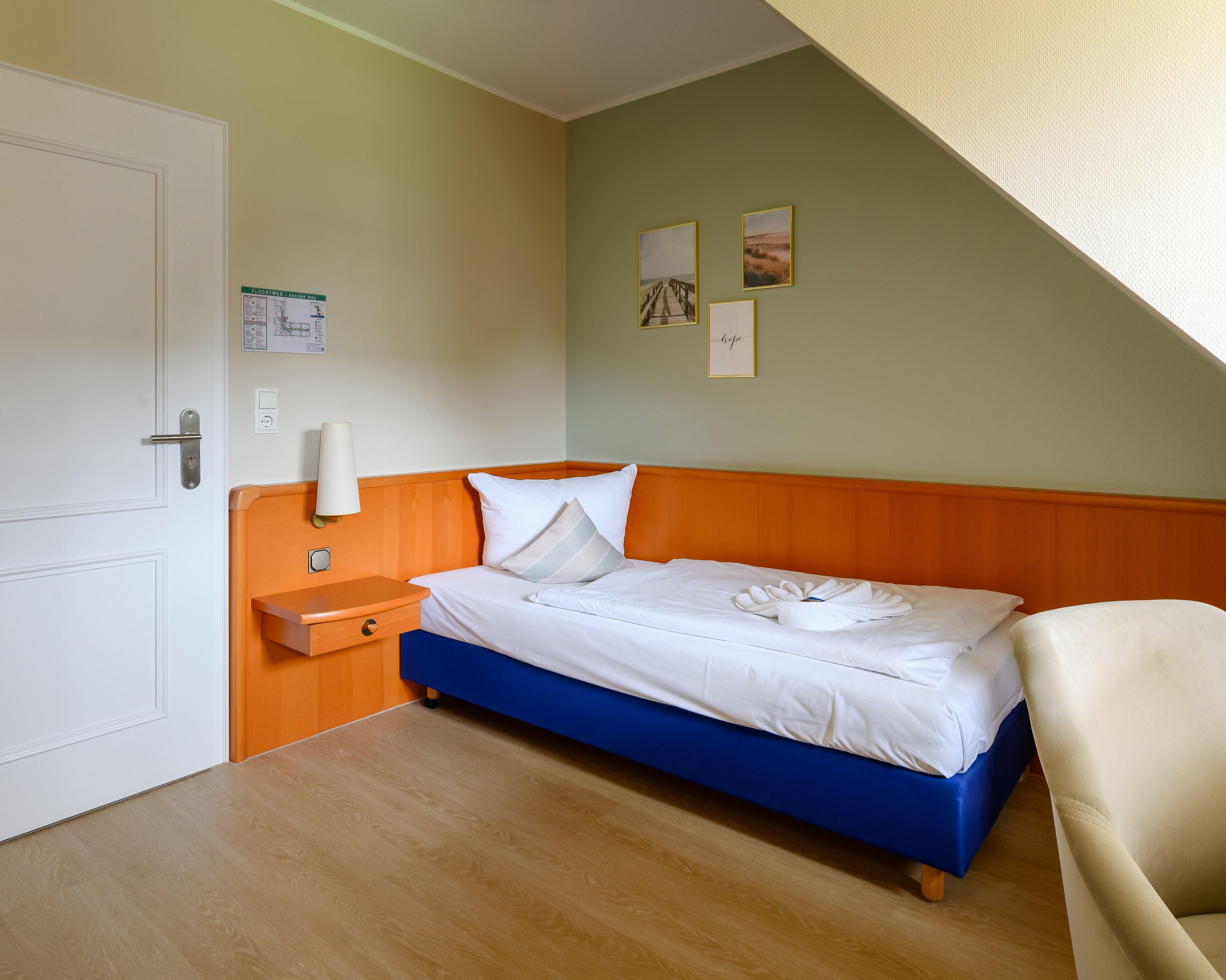 Une chambre à coucher avec un lit, une table de chevet, une lampe et un panneau fixé au mur.
