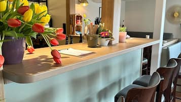 Un área de bar moderna con una barra de madera, taburetes y una maceta con tulipanes amarillos y rojos.