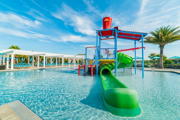 A pool area with a water slide, lounge chairs, and a covered seating area.