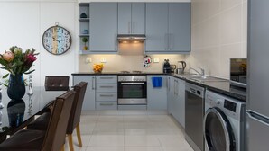 Uma cozinha moderna com armários cinza, forno embutido, máquina de lavar roupa e uma área de jantar com cadeiras e um vaso de flores.