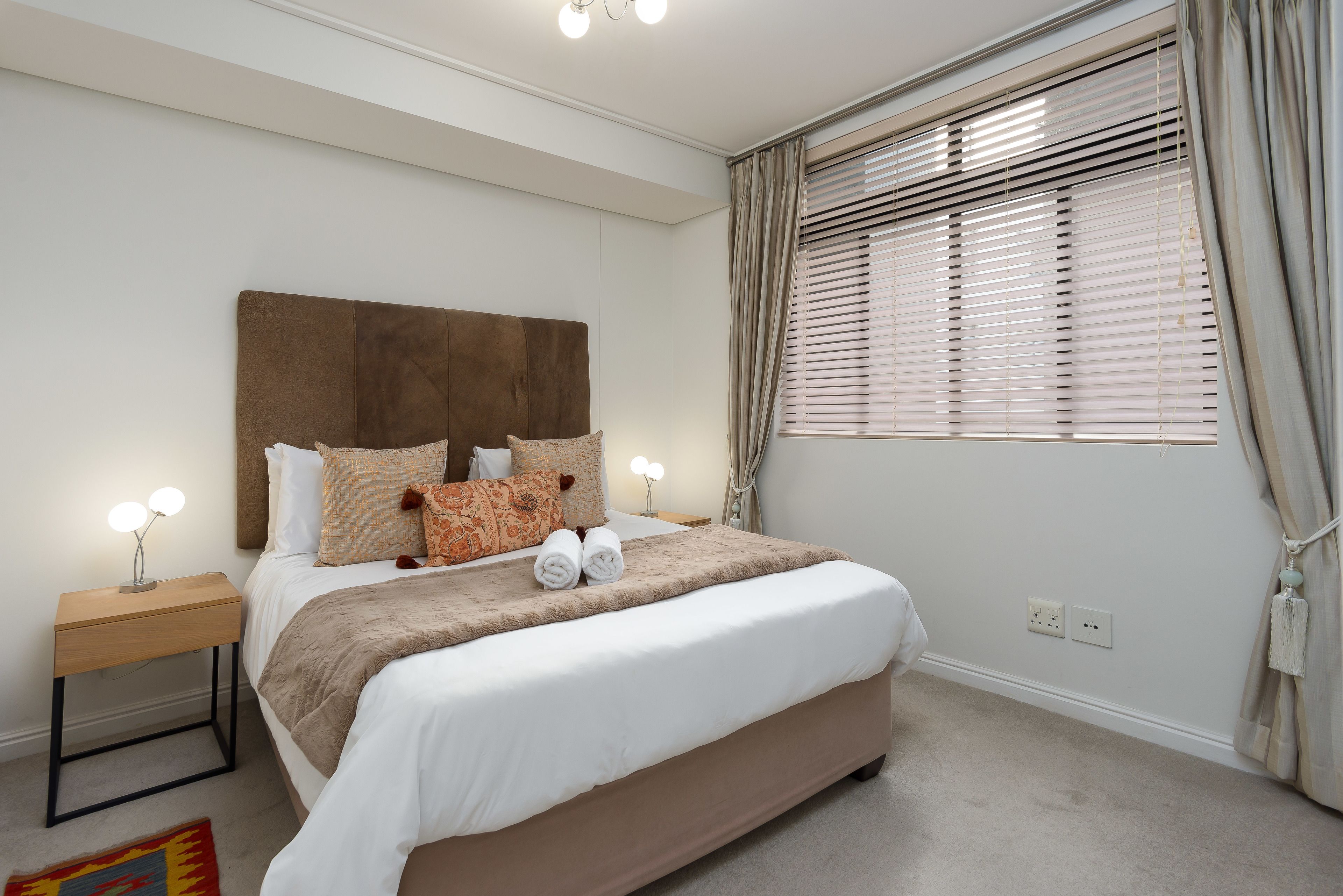 A neatly arranged bedroom with a large bed, bedside lamps, and a window with blinds.