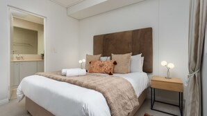 Quarto bem arrumado com uma cama grande, mesas de cabeceira, um criado-mudo, um espelho e uma porta que dá para o banheiro.