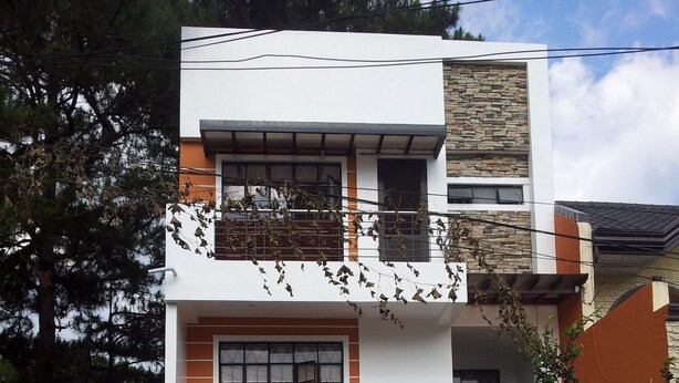 A modern two-story house with a garage, featuring a combination of white and orange walls, a stone facade, and a metal gate.