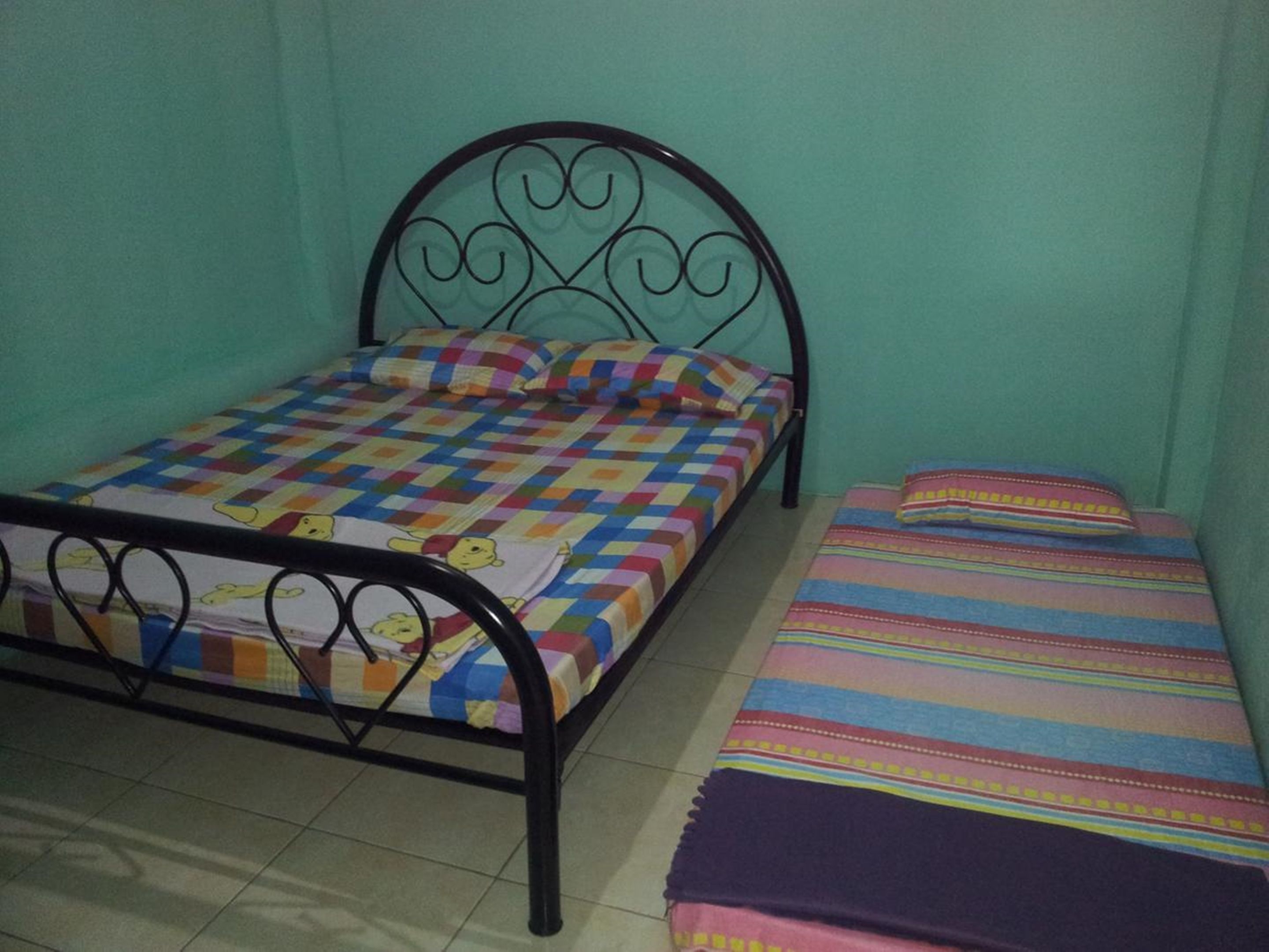 Une petite chambre avec un lit simple, un cadre de lit en métal, une courtepointe aux couleurs vives et une couverture à rayures.