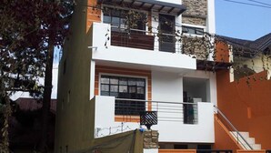 A modern two-story house with a balcony, a staircase, and a gated entrance.