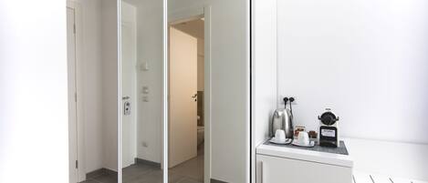 A modern hotel room with a mirrored wardrobe, a small kitchenette with a coffee maker, and a clean, tiled floor.