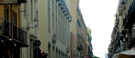 Une rue animée, bordée de bâtiments des deux côtés, avec des balcons et des lampadaires.