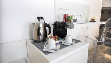 A modern kitchenette with a coffee maker, kettle, and cups on a white countertop.
