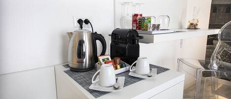 Una kitchenette moderna con cafetera, hervidor y tazas sobre una encimera blanca.