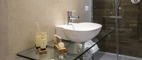 Un baño moderno con tocador de vidrio, lavamanos blanco y cabina de ducha con paredes de vidrio.