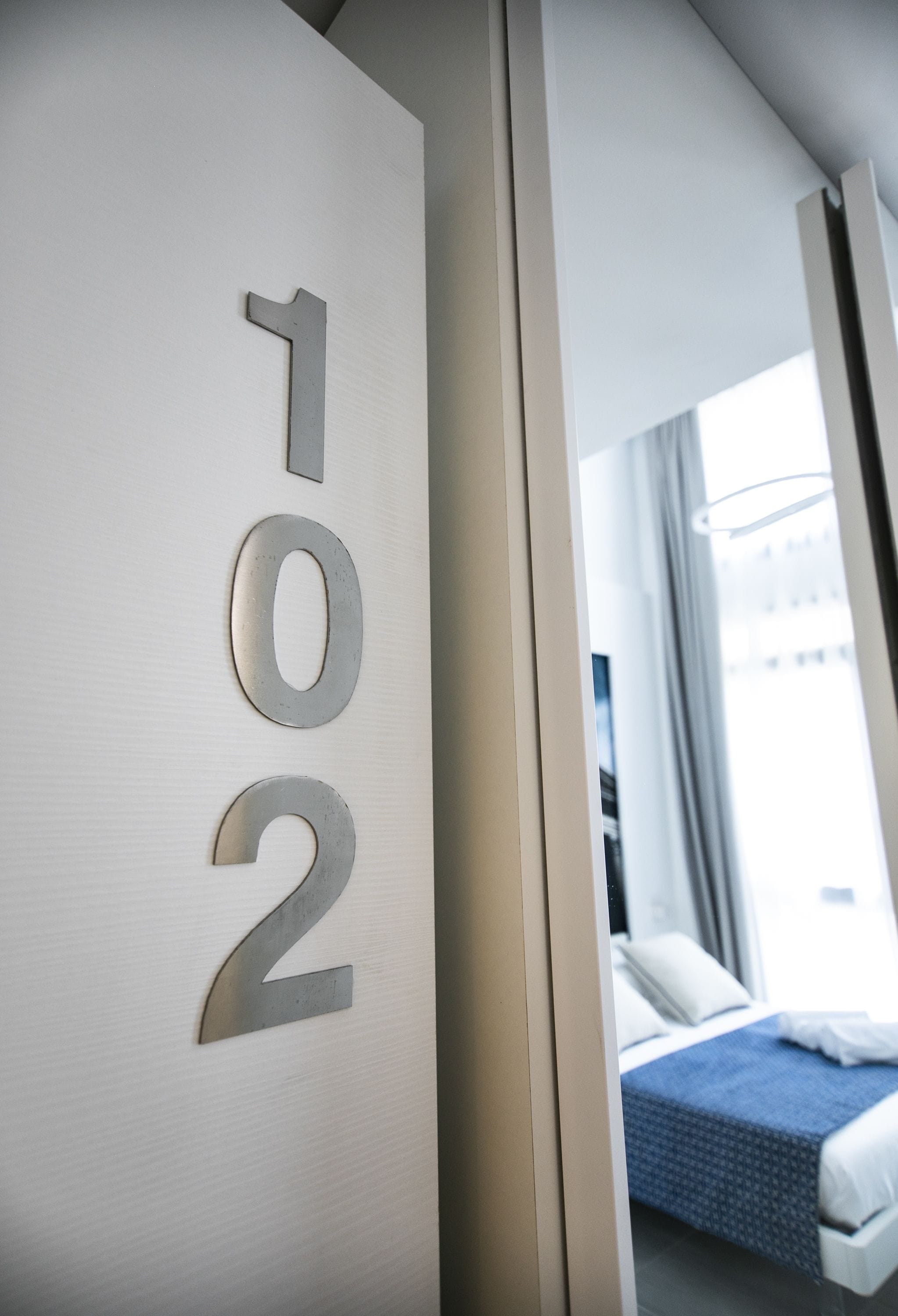 A hotel room with a bed, a window, and a door with the numbers "102" on it.