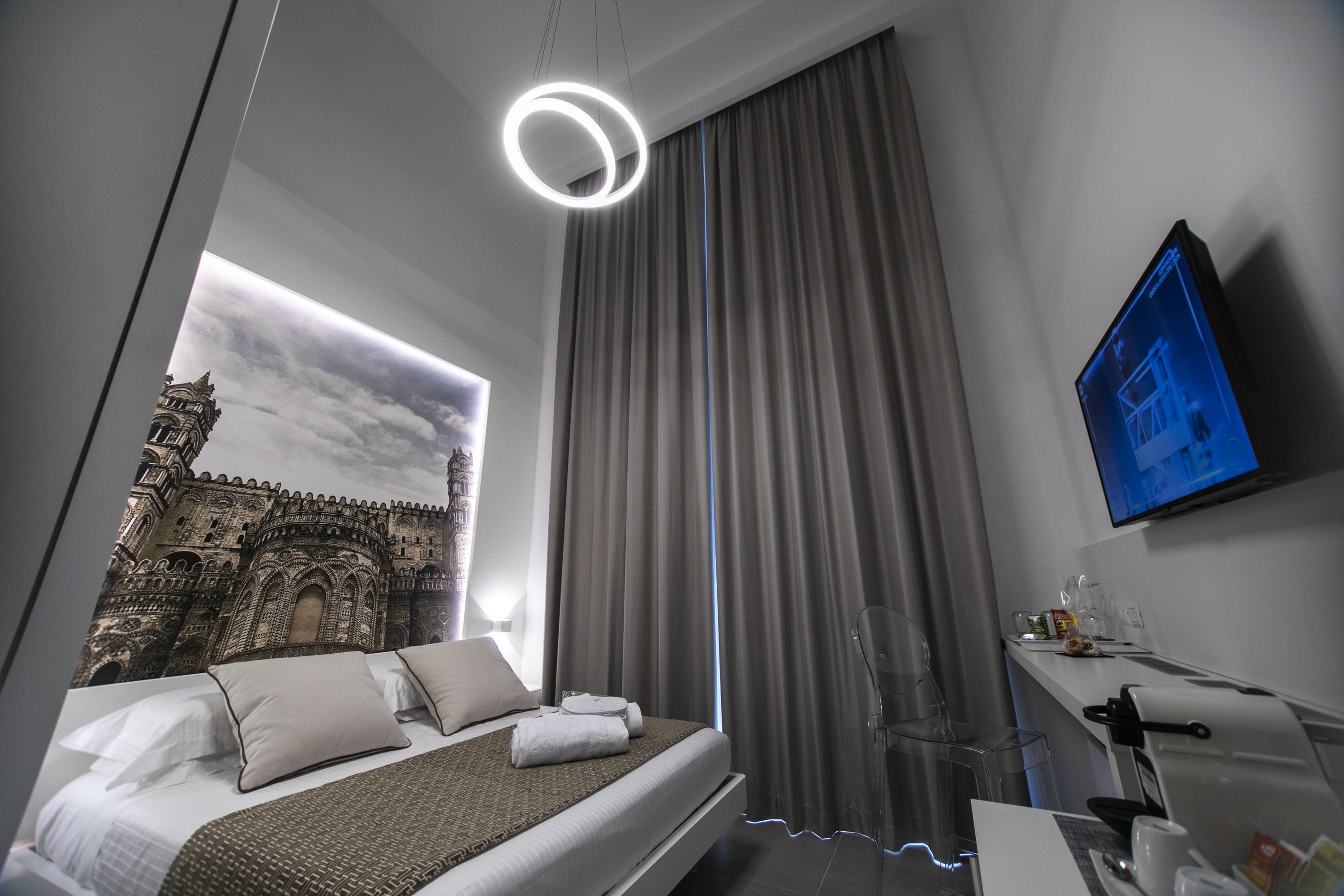 Una moderna camera d'albergo con un letto grande, una TV a schermo piatto, una scrivania con macchina del caffè e vista su un edificio storico dalla finestra.