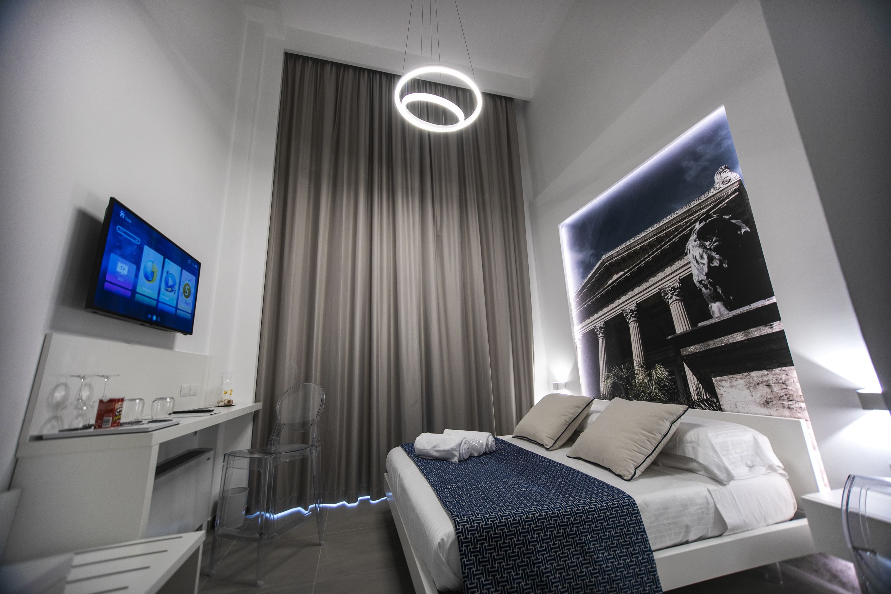 A modern hotel room with a bed, a desk, a TV, and a large window with curtains.