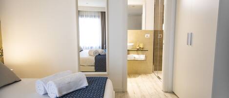 A hotel room with a bed, a bathroom with a shower, and a hallway leading to another room.