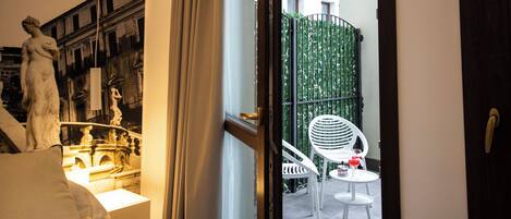 Una habitación de hotel con cama, una estatua, un balcón con sillas y vistas a edificios.