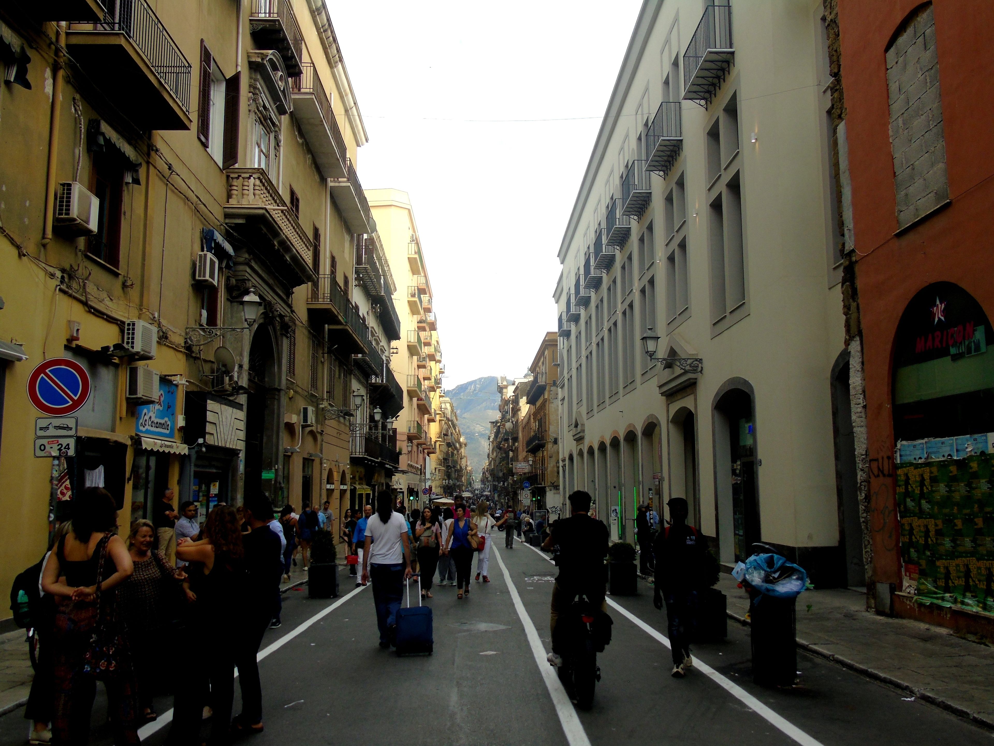 A narrow street lined with multi-story buildings, some with balconies and air conditioning units.
