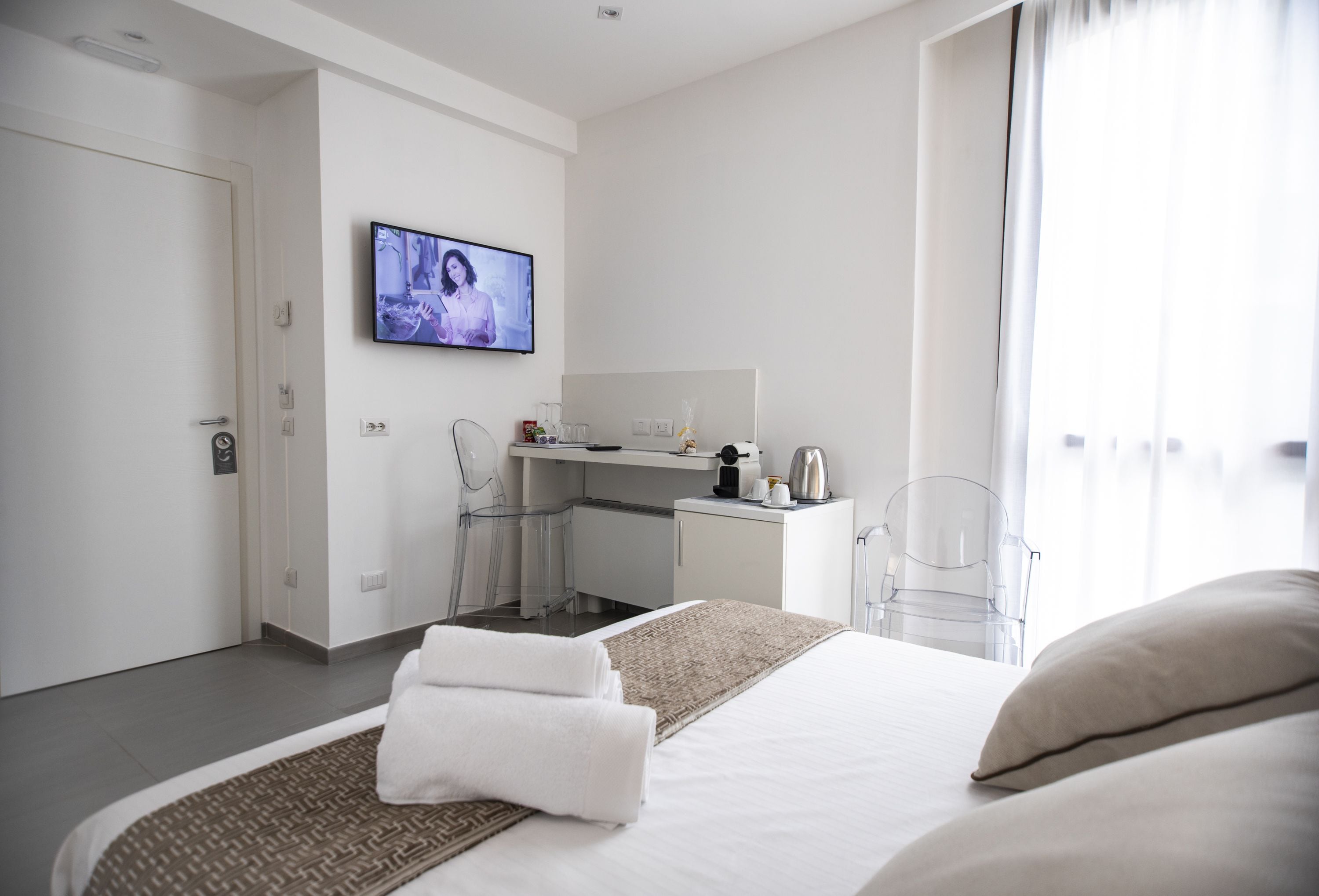 Una habitación de hotel moderna con una cama, un escritorio, televisión y vistas al exterior.