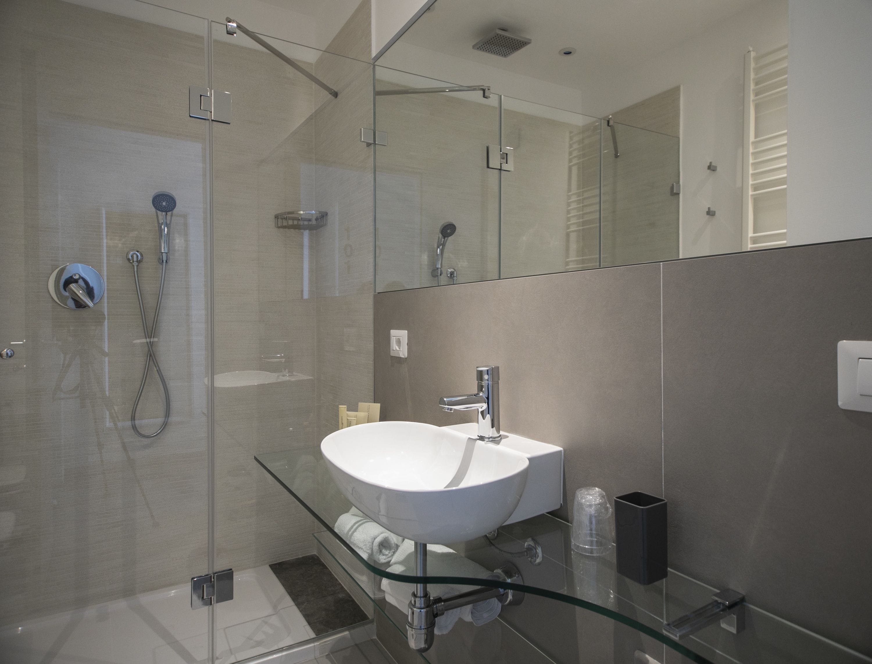 A modern bathroom with a glass shower enclosure, a white sink, and a glass shelf.