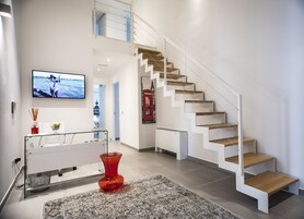 Un interior moderno con una escalera, un televisor de pantalla plana, una mesa de vidrio y un jarrón rojo.