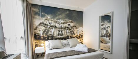 A modern bedroom with a large bed, a nightstand, a mirror, and a wall mural of a historic building.