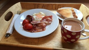 Bandeja de desayuno con huevos, tocino, tomates y tostadas, una taza de té y un tenedor sobre una bandeja de madera.