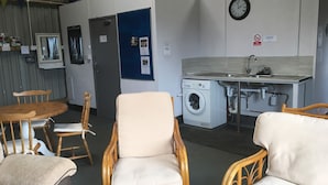 Cocina compacta con lavadora, un lavamanos y un reloj en la pared. Hay sillas de mimbre y una mesa en la zona de comedor.