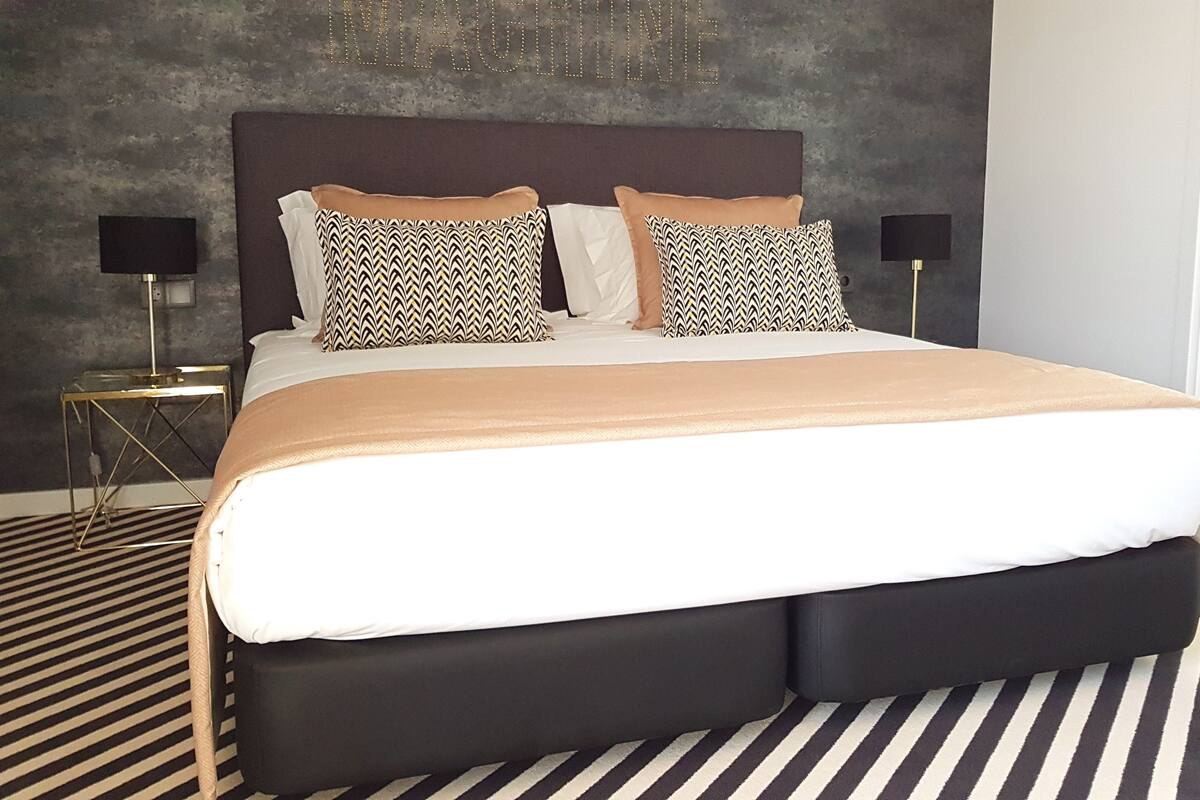 Ein modernes Schlafzimmer mit einem großen Bett, zwei gemusterten Kissen, einem dunklen Kopfteil und einem Streifenboden.