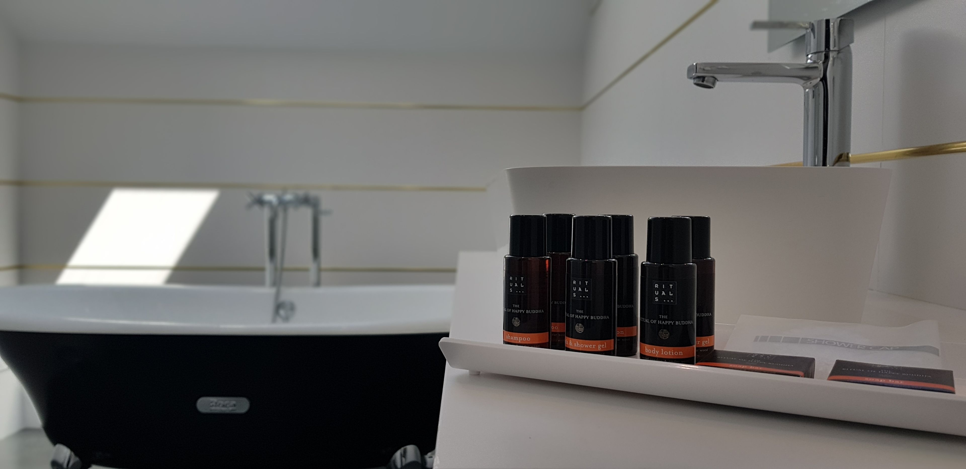 Un baño con una bañera negra, un lavamanos blanco y un estante con botellas de loción corporal y champú.