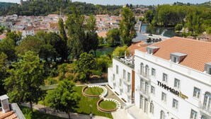 A white building with "THOMAR" on the facade, surrounded by a well-maintained garden with a circular lawn and a small pond. - Thomar Boutique Hotel (Tomar)