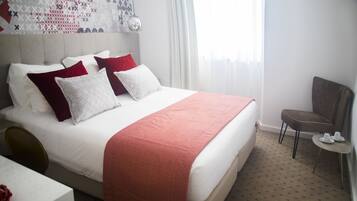 A hotel room with a bed, a chair, a small table, and a wall with a geometric pattern.
