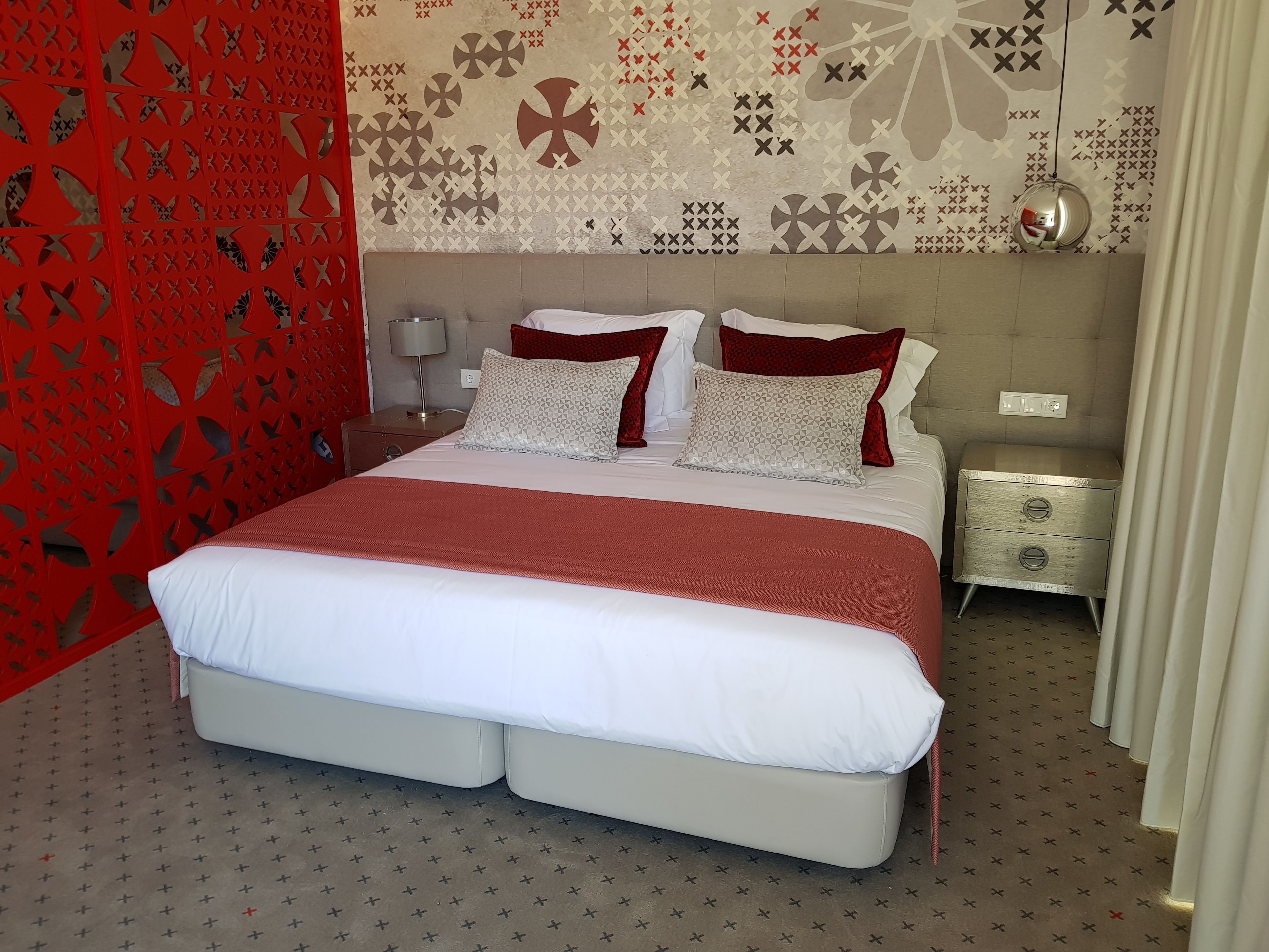 Un dormitorio moderno con una cama grande, dos mesitas de noche y un revistero, además de una pared con diseño.