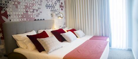 A hotel room with a large bed, a desk, and a patterned wall.