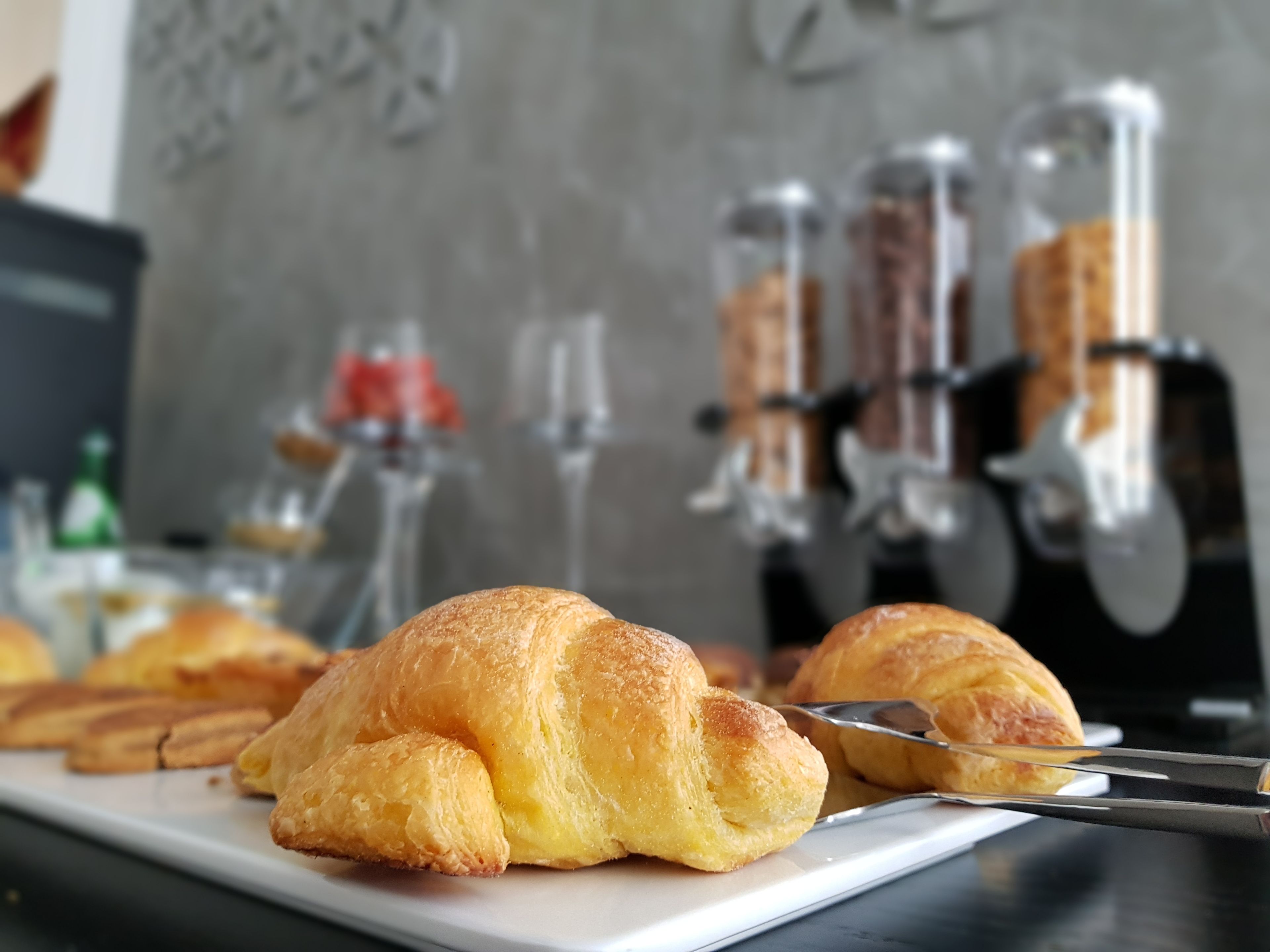 Valkoisella tarjottimella on lautanen täynnä croissantteja, ja sen vieressä on veitsi ja pihdit.