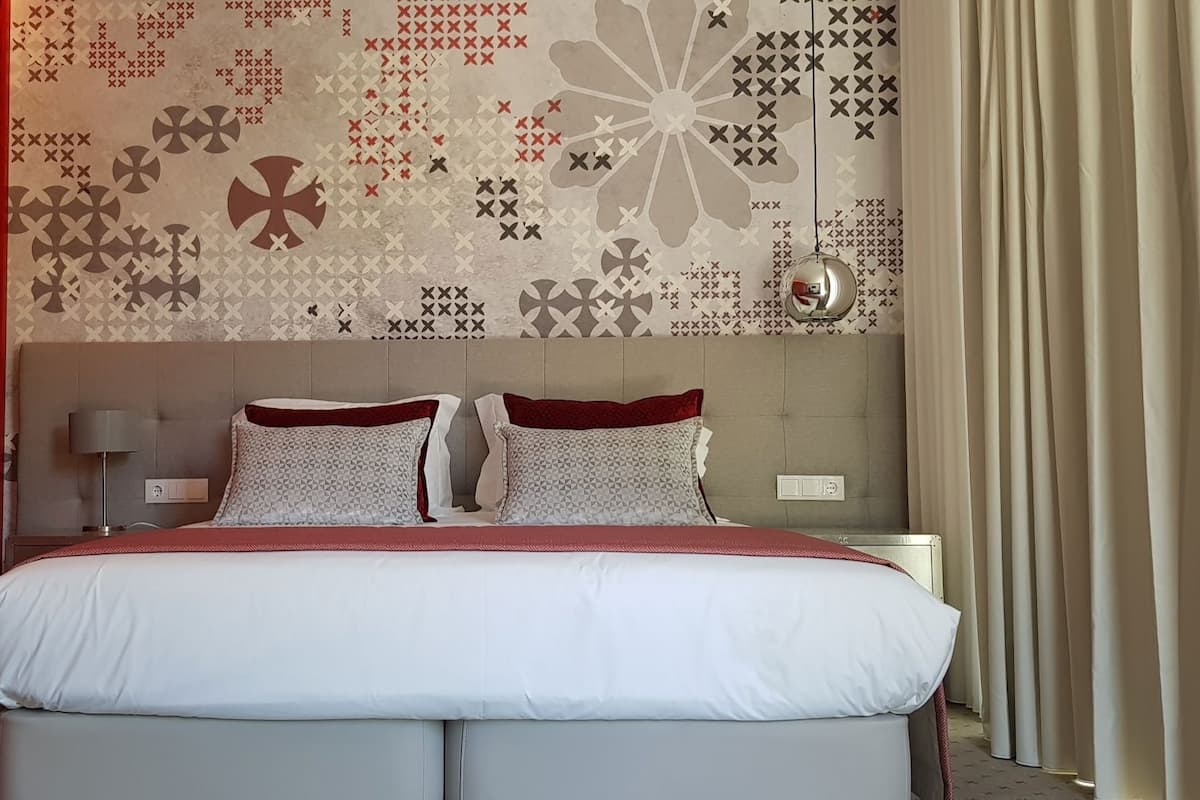 Ein Hotelzimmer mit Bett, Nachttisch, Lampe und einer Wand mit Muster.