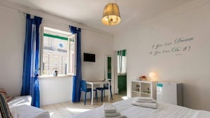 Habitación de hotel con cama, escritorio, silla, televisor y ventana con cortinas azules.