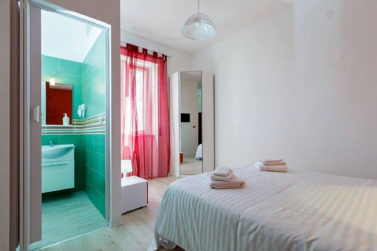 Quarto com cama, mesa de cabeceira, espelho e vista para o banheiro.