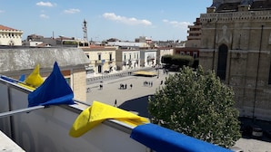 Vista de una plaza urbana con edificios históricos, una torre destacada y un árbol grande.